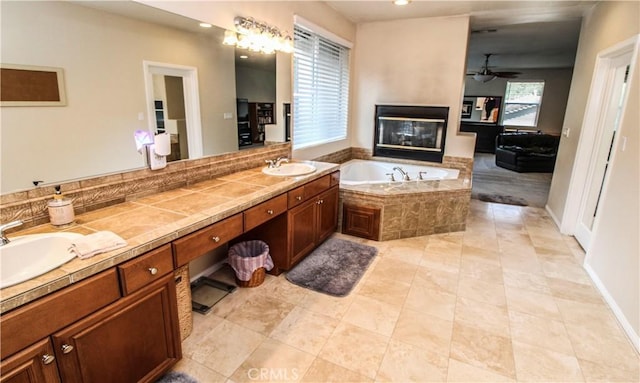 bathroom with a multi sided fireplace, tiled bath, ceiling fan, and vanity