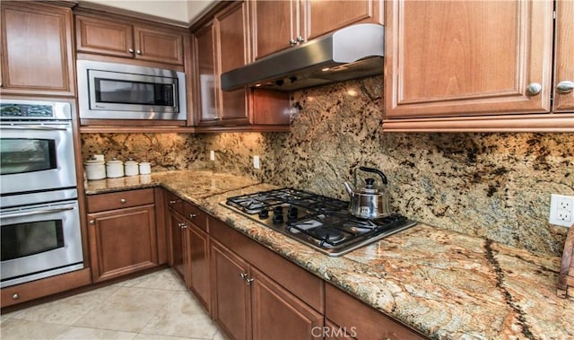 kitchen with light stone countertops, light tile patterned floors, stainless steel appliances, and tasteful backsplash