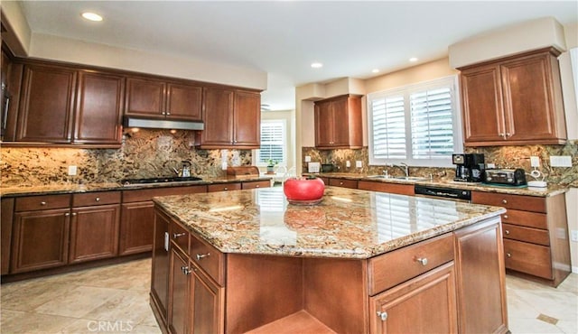 kitchen with light stone countertops, backsplash, a kitchen island, and sink