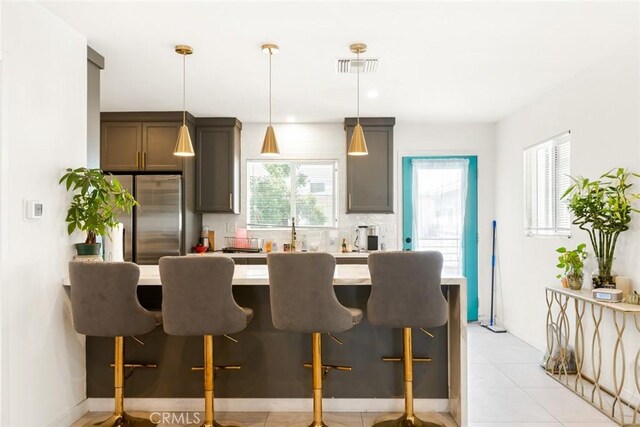 kitchen featuring stainless steel fridge, a kitchen breakfast bar, backsplash, and hanging light fixtures