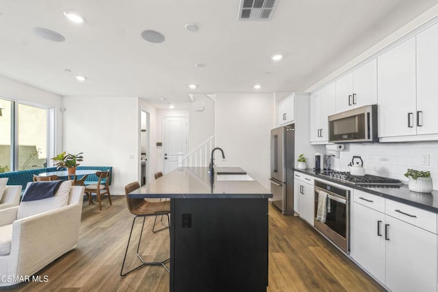 kitchen featuring a kitchen bar, appliances with stainless steel finishes, a kitchen island with sink, dark wood-type flooring, and sink