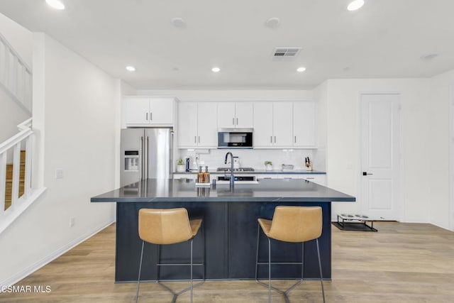 kitchen with white cabinetry, an island with sink, light hardwood / wood-style floors, a breakfast bar area, and appliances with stainless steel finishes