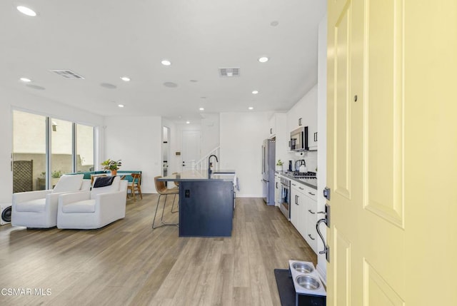 kitchen featuring appliances with stainless steel finishes, a kitchen island with sink, light hardwood / wood-style flooring, white cabinetry, and a breakfast bar area