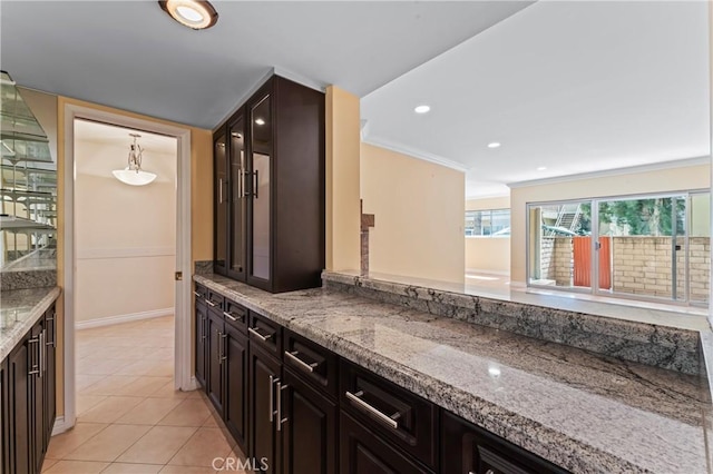 kitchen featuring pendant lighting, dark brown cabinetry, light stone counters, light tile patterned floors, and crown molding