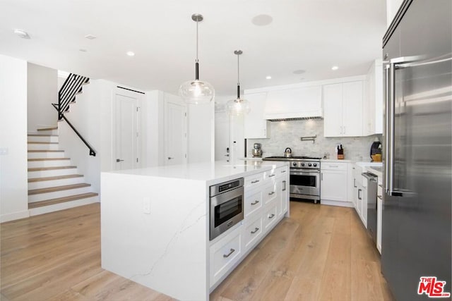 kitchen featuring premium appliances, premium range hood, white cabinetry, and a kitchen island