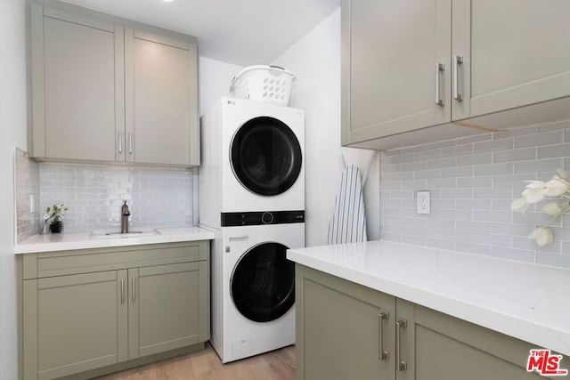 laundry area with light hardwood / wood-style flooring, stacked washer / drying machine, cabinets, and sink