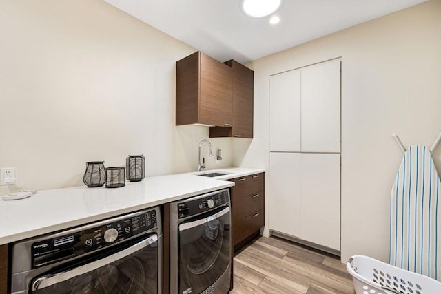 kitchen with dark brown cabinets, sink, light hardwood / wood-style floors, and washer and dryer