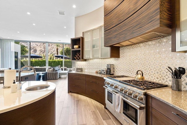 kitchen with custom exhaust hood, light wood-type flooring, sink, range with two ovens, and light stone countertops