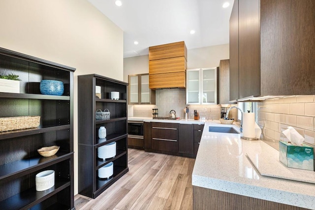 kitchen featuring light stone counters, sink, light hardwood / wood-style flooring, black microwave, and decorative backsplash