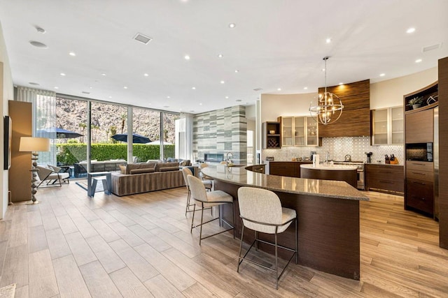 kitchen featuring light stone counters, tasteful backsplash, a breakfast bar, pendant lighting, and light hardwood / wood-style flooring