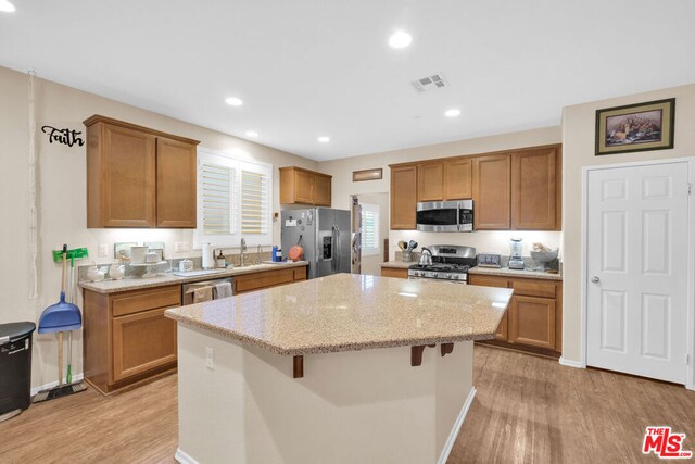 kitchen featuring light stone counters, stainless steel appliances, light wood-type flooring, a kitchen bar, and a center island