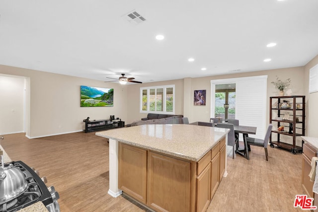 kitchen featuring light hardwood / wood-style floors, a kitchen island, light stone countertops, and ceiling fan