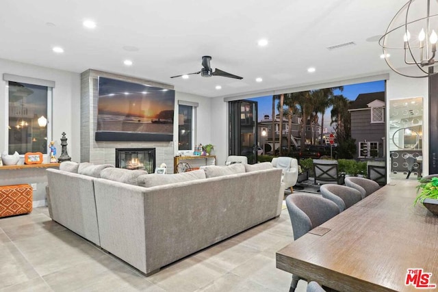 living room with ceiling fan with notable chandelier and a large fireplace