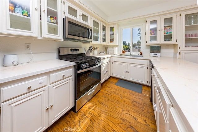 kitchen featuring light stone counters, sink, white cabinetry, light hardwood / wood-style flooring, and stainless steel appliances