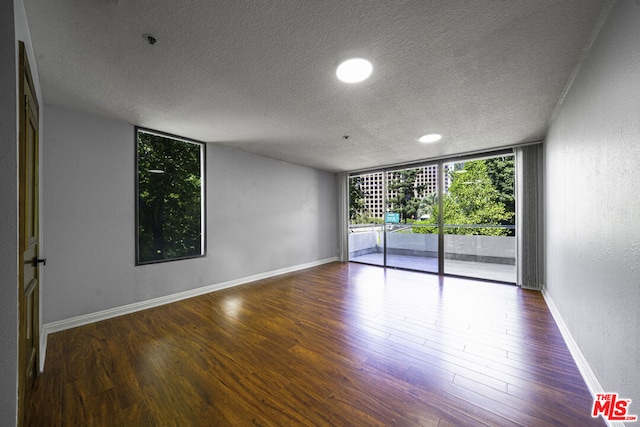 empty room with a textured ceiling, dark hardwood / wood-style floors, and expansive windows