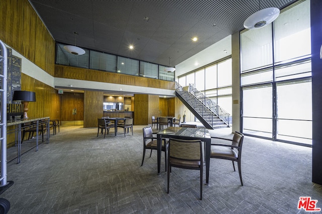 carpeted dining area featuring a high ceiling and wood walls