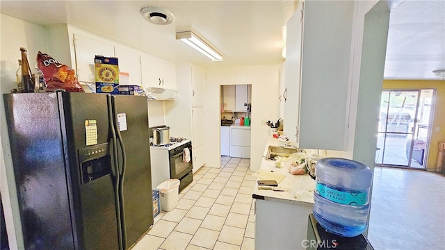 kitchen with white gas range oven, white cabinets, black fridge, exhaust hood, and washing machine and clothes dryer