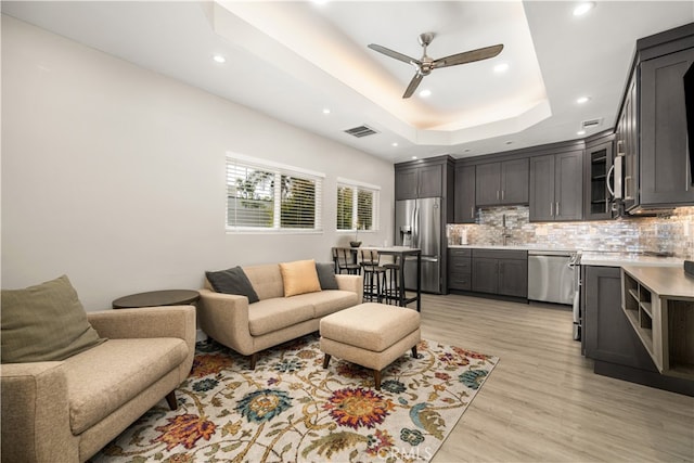 living room with ceiling fan, sink, light hardwood / wood-style flooring, and a tray ceiling