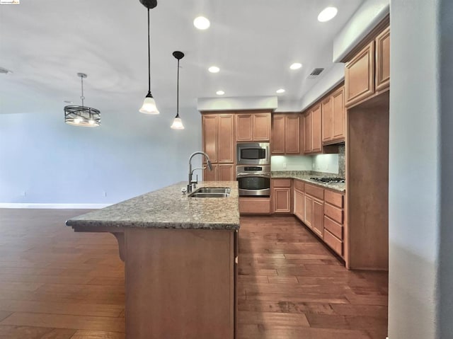 kitchen with hanging light fixtures, sink, light stone countertops, appliances with stainless steel finishes, and dark hardwood / wood-style flooring