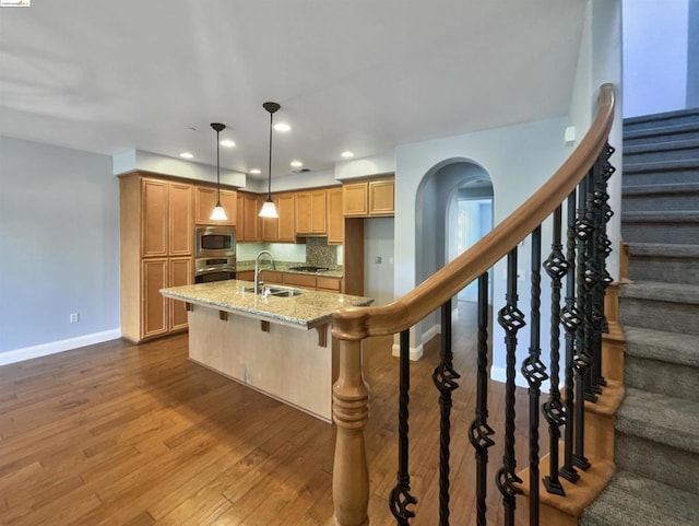 kitchen featuring dark hardwood / wood-style flooring, light stone counters, stainless steel appliances, sink, and hanging light fixtures