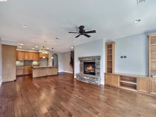 unfurnished living room featuring a stone fireplace, ceiling fan, sink, and wood-type flooring