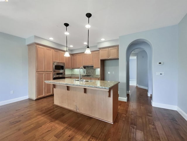 kitchen featuring light stone countertops, light brown cabinetry, dark wood-type flooring, and a center island with sink