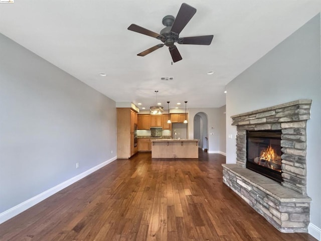 unfurnished living room with a stone fireplace, ceiling fan, and dark hardwood / wood-style floors