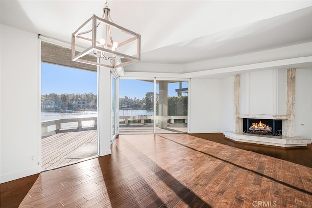 unfurnished living room featuring a wall of windows, a water view, a fireplace, an inviting chandelier, and hardwood / wood-style floors