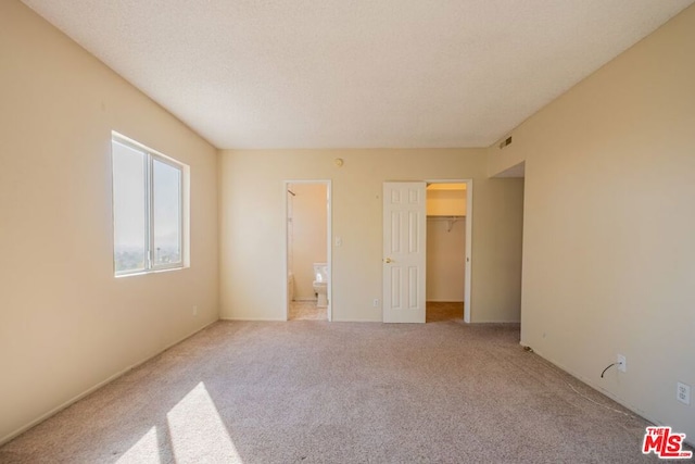 unfurnished bedroom with a walk in closet, light carpet, connected bathroom, and a closet