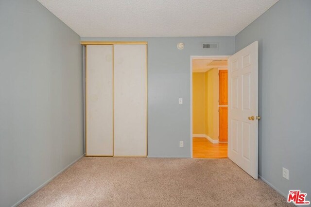 unfurnished bedroom featuring a textured ceiling, light carpet, and a closet