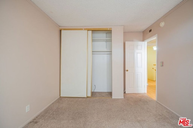 unfurnished bedroom featuring crown molding, a textured ceiling, light carpet, and a closet