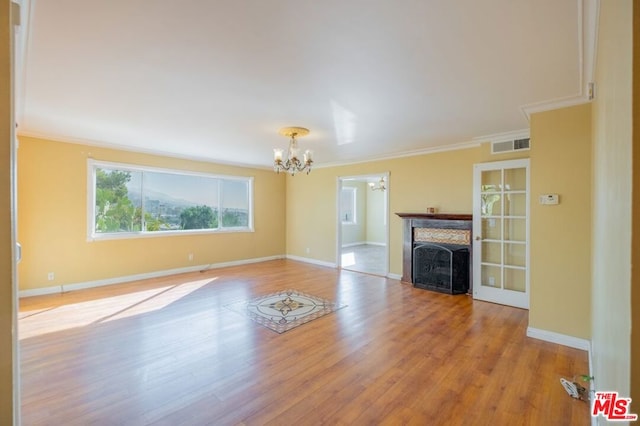 unfurnished living room with a chandelier, ornamental molding, and light hardwood / wood-style flooring