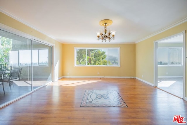 spare room featuring wood-type flooring, ornamental molding, and an inviting chandelier