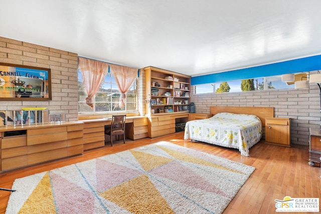 bedroom featuring built in desk, brick wall, and light wood-type flooring