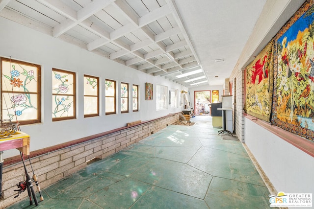 hallway with brick wall and vaulted ceiling with beams