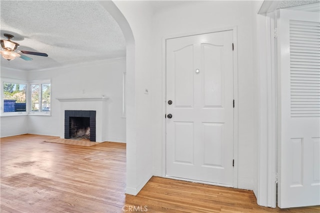 entryway featuring ceiling fan, wood-type flooring, crown molding, a fireplace, and a textured ceiling