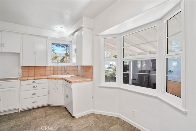 kitchen with white cabinets, tile countertops, backsplash, and sink