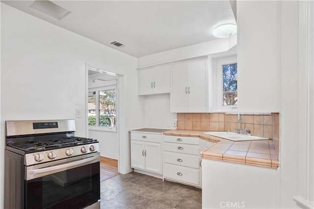 kitchen featuring sink, stainless steel gas range, white cabinetry, tile counters, and backsplash