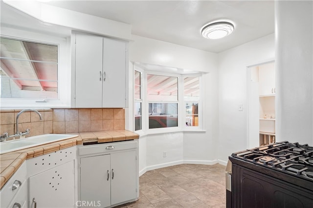 kitchen with range with gas cooktop, sink, tile countertops, backsplash, and white cabinets