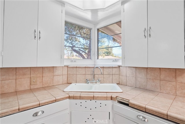 kitchen featuring tasteful backsplash, white cabinetry, sink, and tile counters