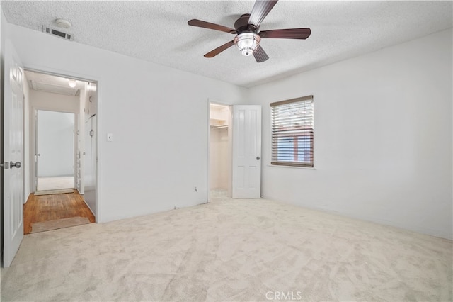 unfurnished bedroom with a walk in closet, ceiling fan, light carpet, a closet, and a textured ceiling