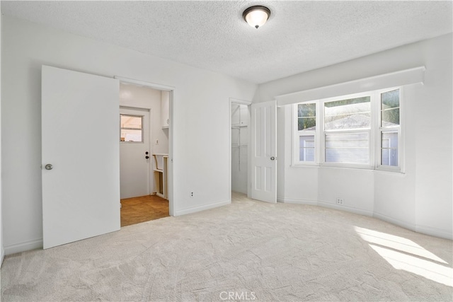 unfurnished bedroom featuring light colored carpet, connected bathroom, multiple windows, and a textured ceiling