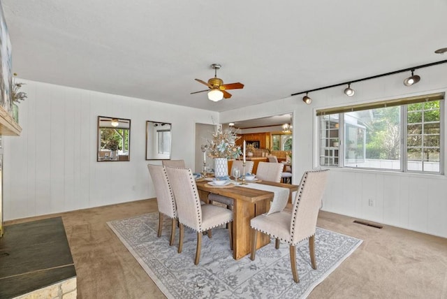 dining space with wooden walls, light carpet, and ceiling fan