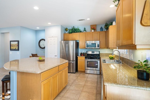 kitchen featuring a center island, sink, light stone countertops, light tile patterned flooring, and stainless steel appliances