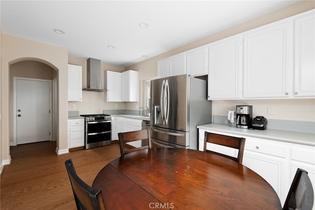 kitchen featuring sink, wall chimney exhaust hood, stainless steel appliances, white cabinets, and hardwood / wood-style flooring