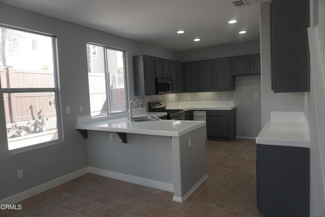 kitchen with a breakfast bar, sink, gray cabinets, appliances with stainless steel finishes, and kitchen peninsula