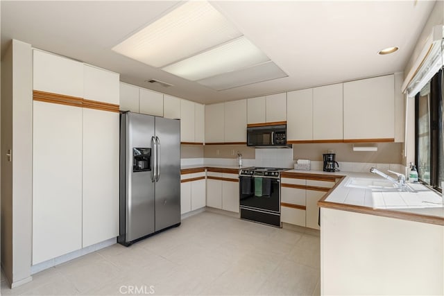 kitchen featuring stainless steel fridge, sink, white cabinetry, tile counters, and range with electric cooktop