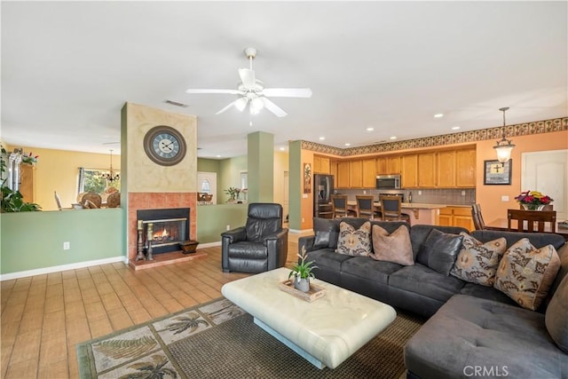 living room with light hardwood / wood-style floors, ceiling fan, and a tiled fireplace