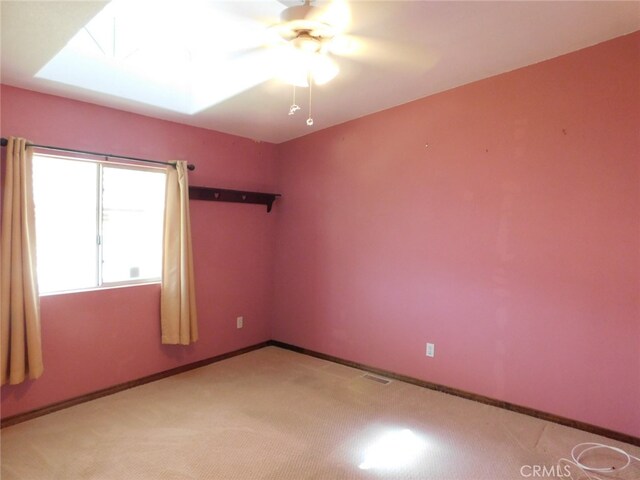 empty room featuring light carpet, ceiling fan, and a skylight