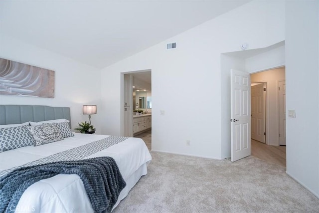 bedroom featuring light carpet, ensuite bathroom, and lofted ceiling